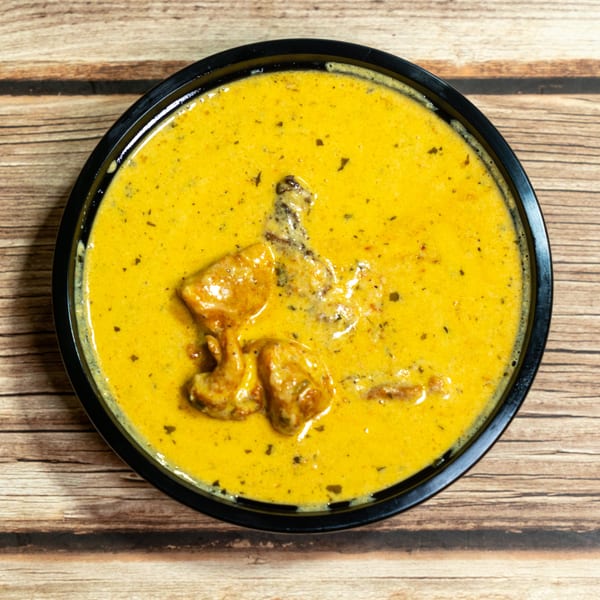 Overhead view of a black bowl filled with creamy yellow chicken curry on a wooden table.