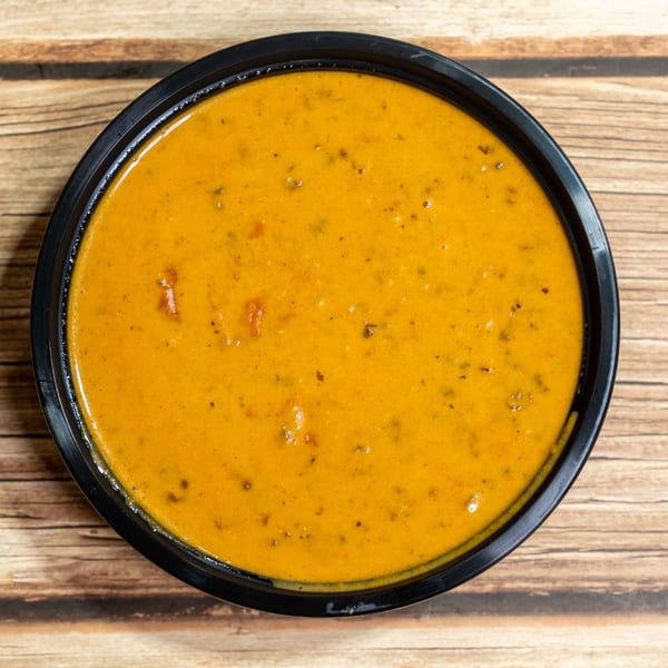 Overhead view of a black bowl filled with a rich orange-yellow curry on a wooden surface.