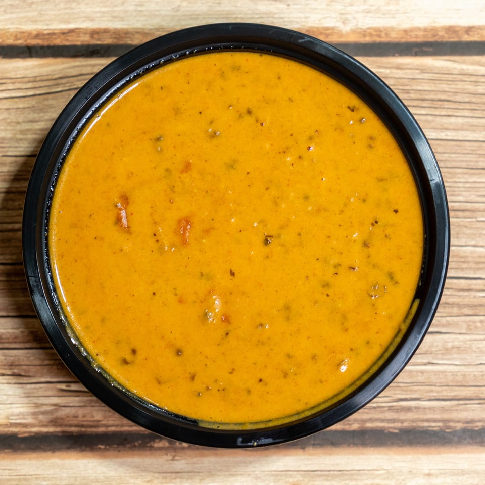 Overhead view of a black bowl filled with a rich orange-yellow curry on a wooden surface.