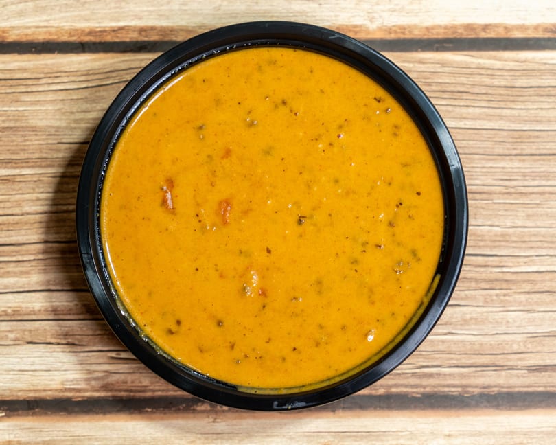 Overhead view of a black bowl filled with a rich orange-yellow curry on a wooden surface.