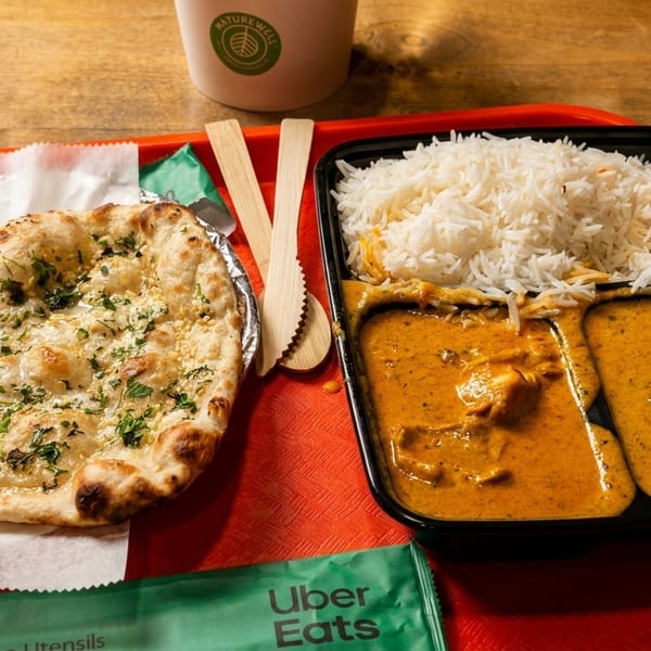 Indian takeout meal with naan bread, rice, and two curries on a red tray.