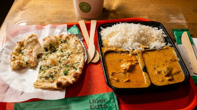 Indian takeout meal with naan bread, rice, and two curries on a red tray.