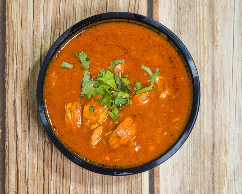 Overhead view of a black bowl filled with orange curry, garnished with fresh green cilantro.