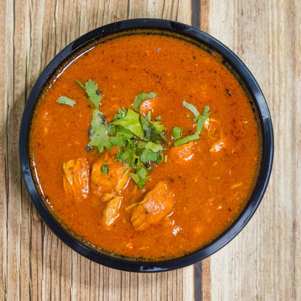 Overhead view of a black bowl filled with orange curry, garnished with fresh green cilantro.