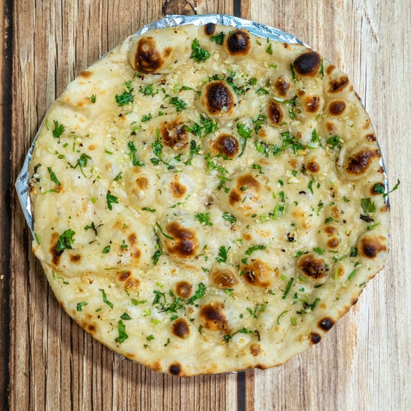 Garlic naan bread with fresh herbs and charred spots on a wooden surface.