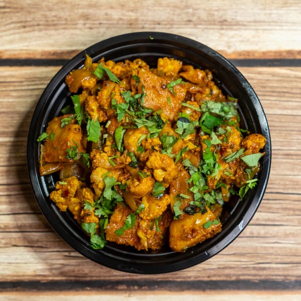 A black bowl filled with Aloo Gobi, a vibrant Indian dish of spiced potatoes and cauliflower, garnished with fresh cilantro.