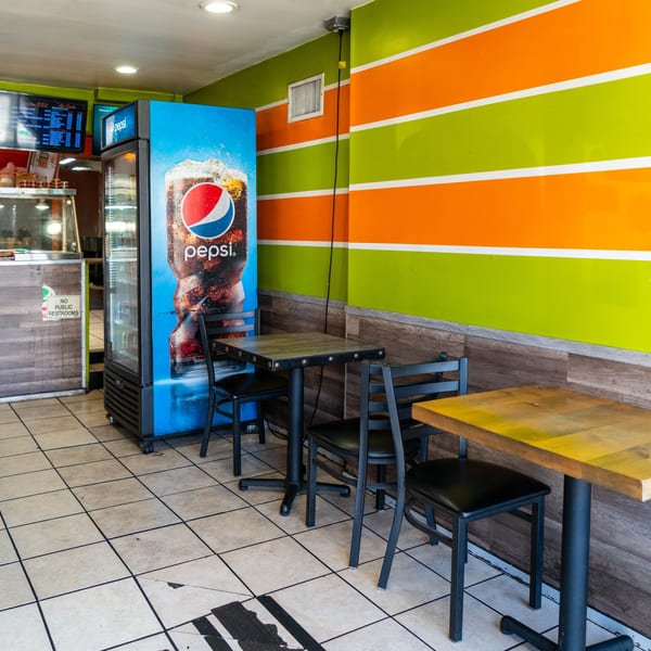 Restaurant interior with green and orange striped walls, a Pepsi cooler, and several tables with chairs.
