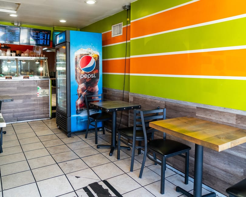 Restaurant interior with green and orange striped walls, a Pepsi cooler, and several tables with chairs.