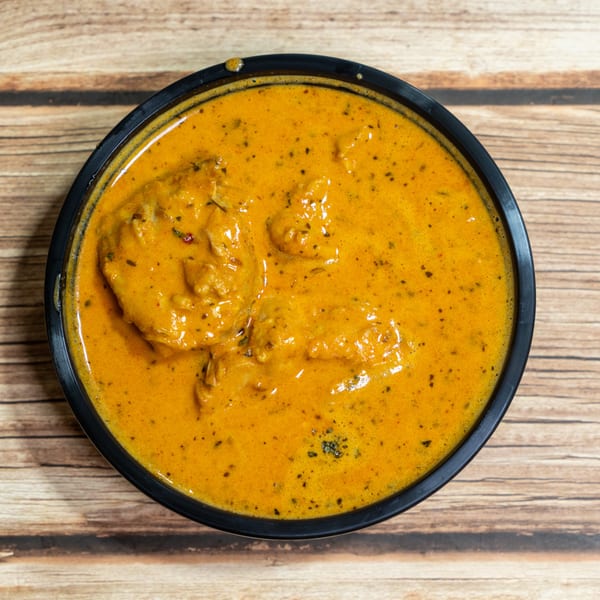 Overhead view of a black bowl filled with creamy orange butter chicken on a wooden table.