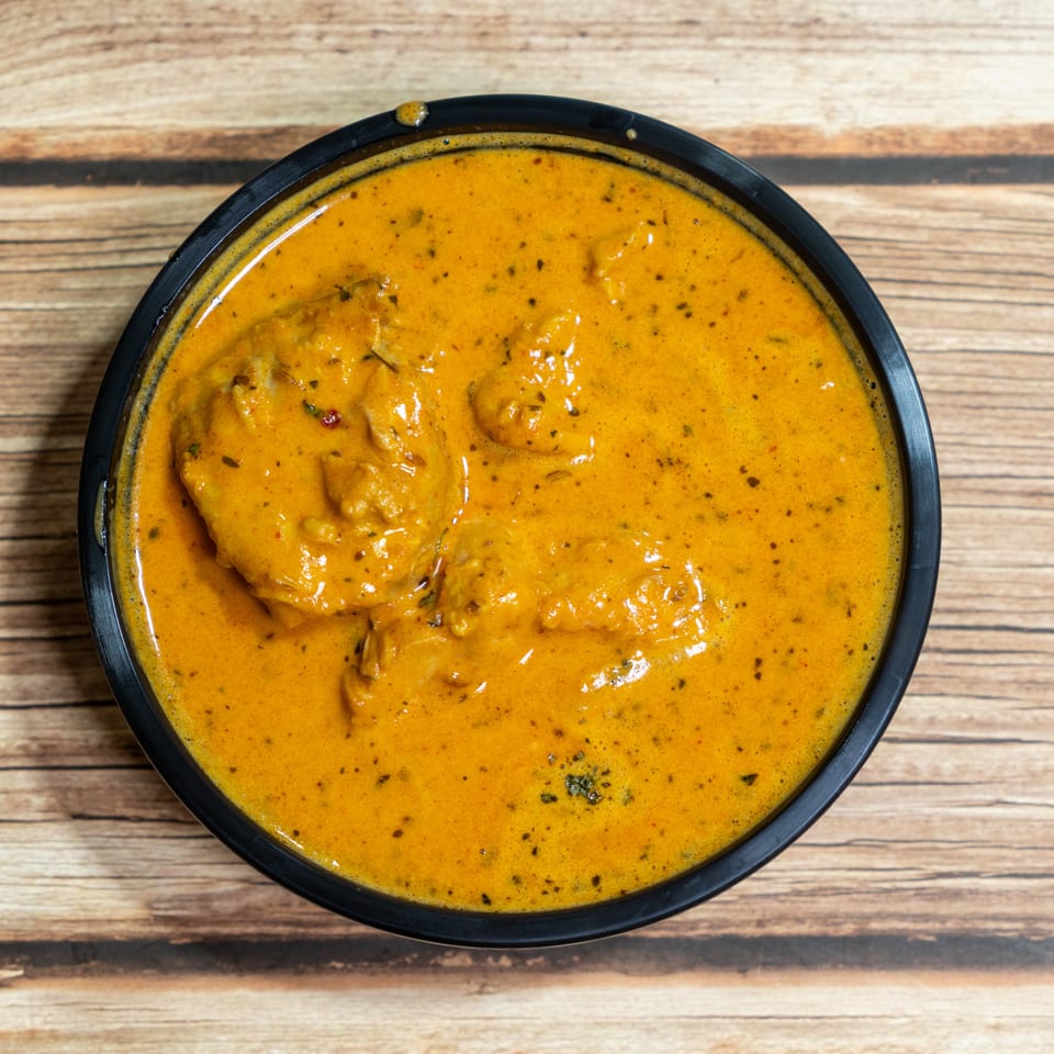 Overhead view of a black bowl filled with creamy orange butter chicken on a wooden table.