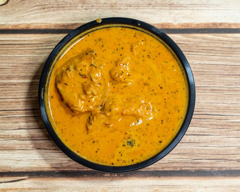 Overhead view of a black bowl filled with creamy orange butter chicken on a wooden table.