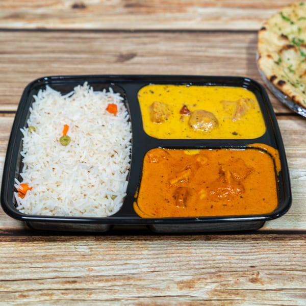 Indian takeout meal with white rice, two curries, and naan bread on a wooden table.