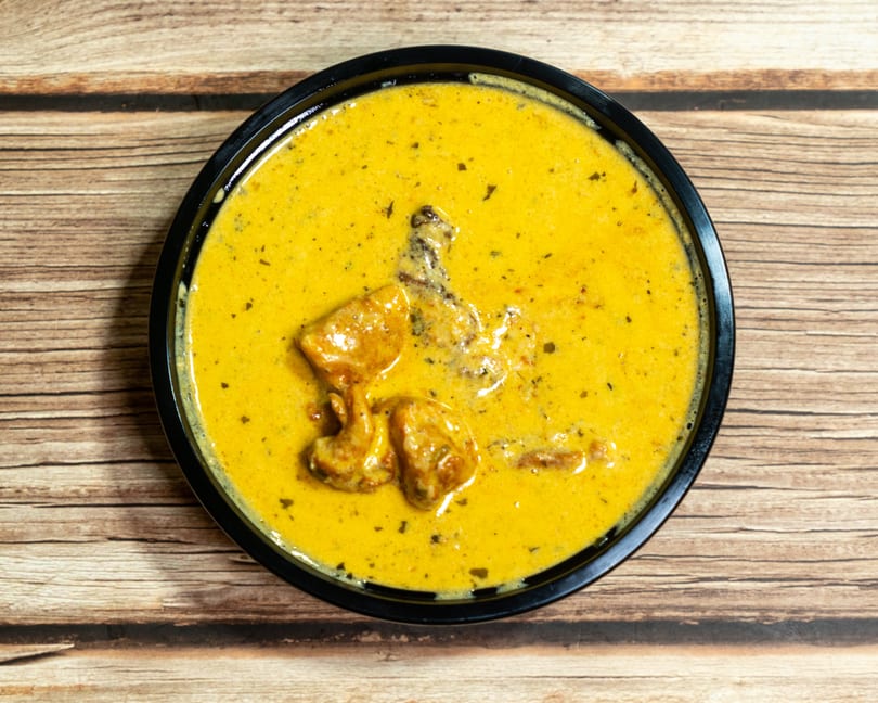 Overhead view of a black bowl filled with creamy yellow chicken curry on a wooden table.