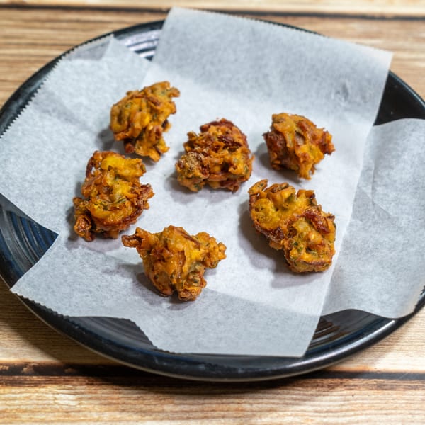 Six golden-brown pakoras, a fried Indian snack, on white parchment paper in a black bowl.
