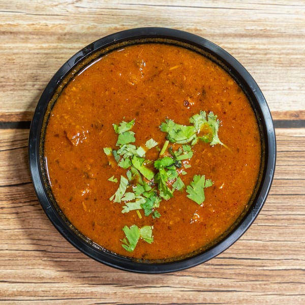 Overhead view of a black bowl filled with a rich, reddish-brown curry, garnished with fresh cilantro.