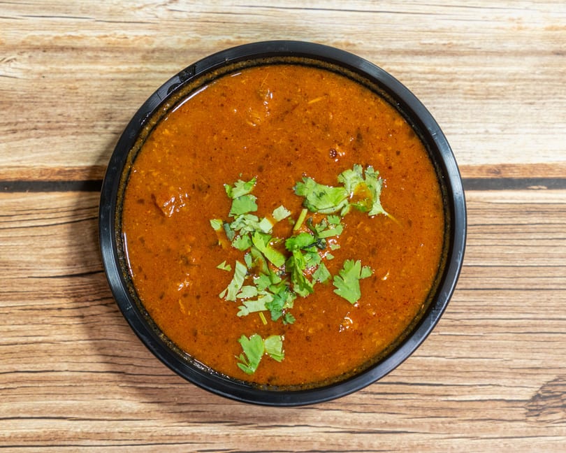 Overhead view of a black bowl filled with a rich, reddish-brown curry, garnished with fresh cilantro.